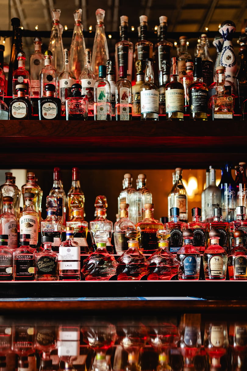 A large collection of tequila bottles, including Don Julio and Teremana, displayed on shelves.